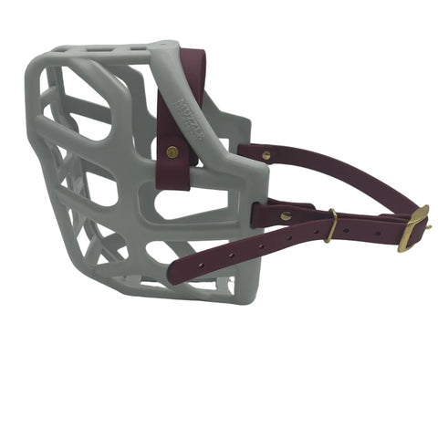 The Muzzle Movement Grey Taz dog muzzle with wine straps and brass hardware on a white background
